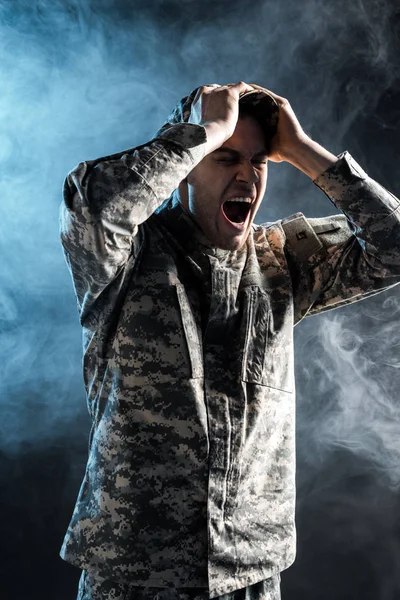 Soldado emocional en uniforme militar gritando en negro con humo - foto de stock