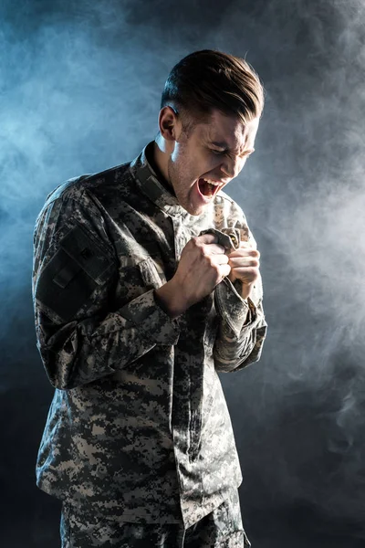 Emotional man in military uniform screaming on black with smoke — Stock Photo