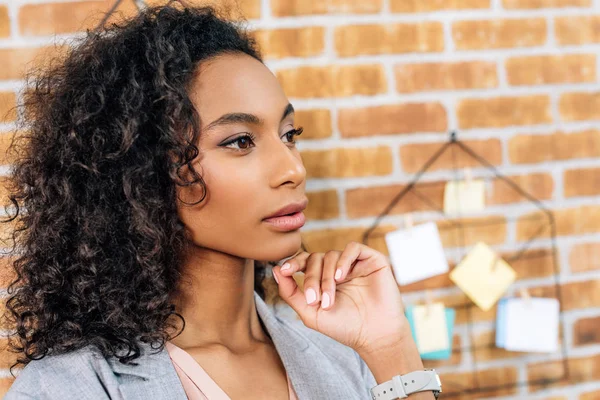 Reflexiva afroamericana casual mujer de negocios tocando la barbilla en la oficina loft - foto de stock