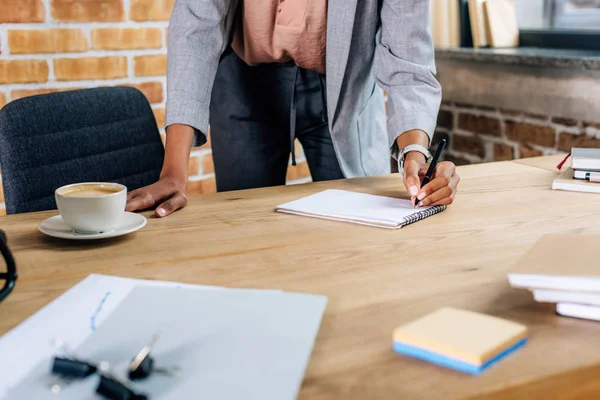 Cropped view of african american Casual businesswoman writing in notebook at table in loft office — Stock Photo