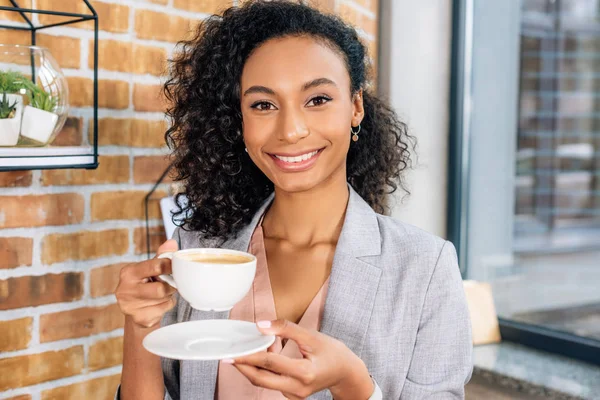 Schöne lächelnde afrikanisch-amerikanische Geschäftsfrau mit Kaffeetasse im Büro — Stockfoto