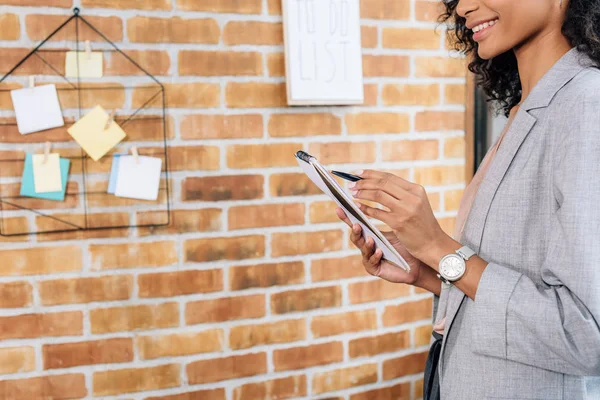 Teilansicht einer afrikanisch-amerikanischen Gelegenheitsunternehmerin, die im Loft-Büro in Notizbuch schreibt — Stockfoto