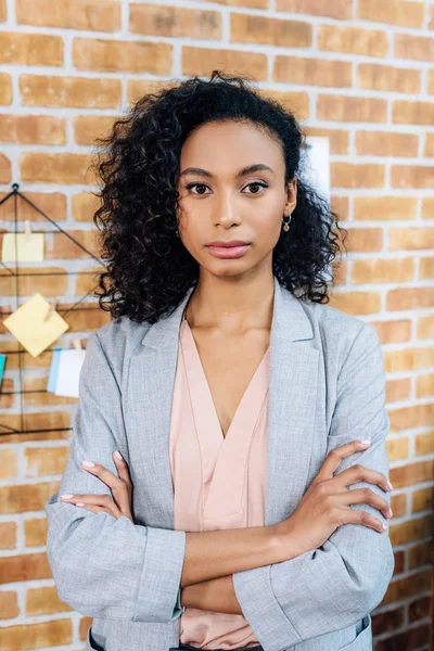Confiada afroamericana Casual mujer de negocios con brazos cruzados en la oficina loft - foto de stock