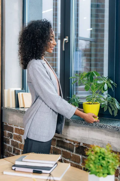 African american Casual businesswoman holding flowerpot with plant in loft office — Stock Photo
