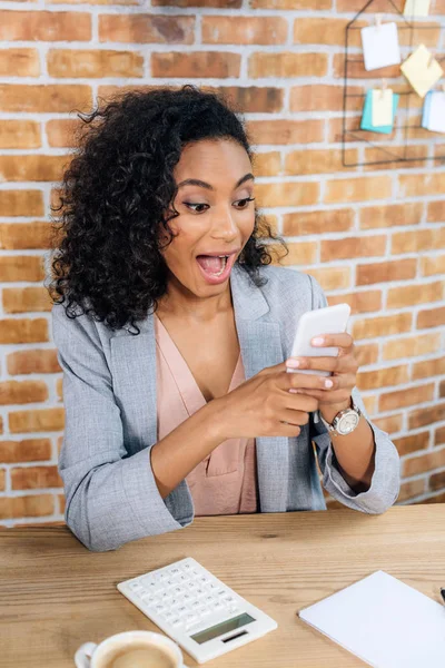 Excited african american Casual businesswoman using smartphone at desk — Stock Photo