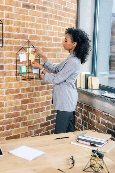Casual african american businesswoman hanging Sticky Notes with pins in loft office — Stock Photo