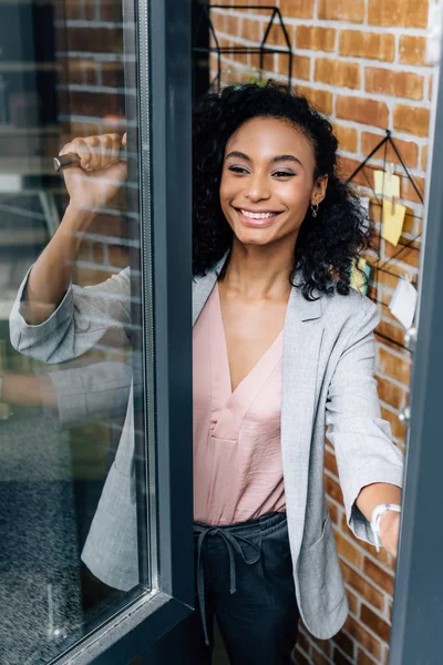 Sonriente afroamericano casual mujer de negocios ventana de apertura en la oficina loft - foto de stock