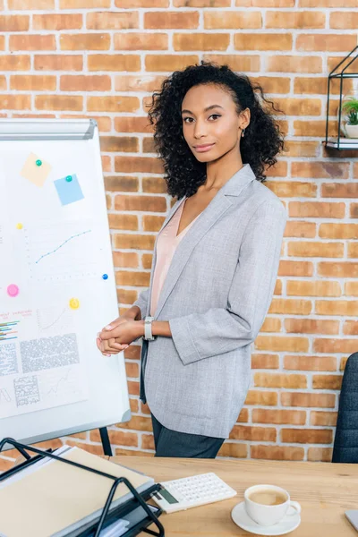 Beautiful african american Casual businesswoman near flipchart looking at camera in loft office — Stock Photo