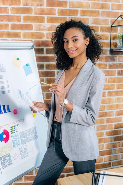 Smiling african american Casual businesswoman posing near flipchart in loft office — Stock Photo
