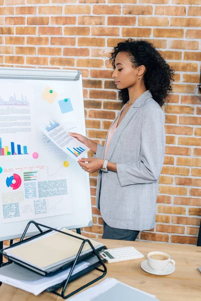 Mujer de negocios ocasional afroamericana cerca de flipchart con papel durante la presentación en la oficina loft - foto de stock