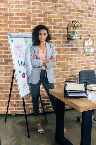 African american Casual businesswoman with crossed arms near flipchart during Presentation in loft office — Stock Photo