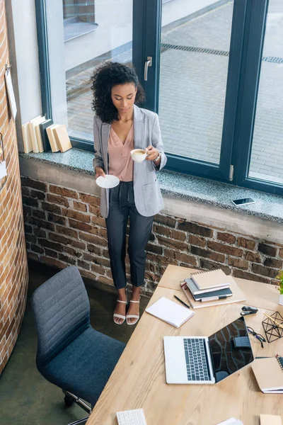 Beautiful african american Casual businesswoman with coffee cup near office desk with laptop — Stock Photo