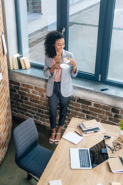 Hochwinkel-Ansicht der schönen afrikanisch-amerikanischen Gelegenheitsunternehmerin in der Nähe von Büroschreibtisch mit Laptop — Stockfoto