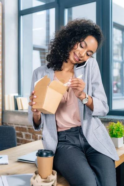 African american Casual businesswoman with Take Out Box and chopsticks talking on smartphone — Stock Photo