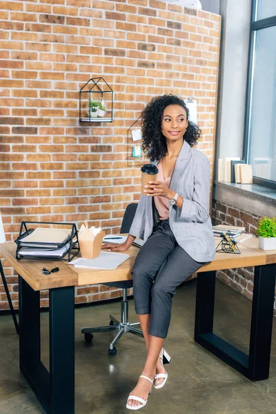 Africano americano Casual empresária sentada na mesa com café para ir e takeaway box no escritório — Fotografia de Stock