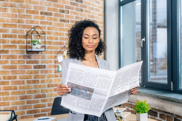 Attraktive afrikanisch-amerikanische Gelegenheitsunternehmerin liest Wirtschaftszeitung im Loft-Büro — Stockfoto