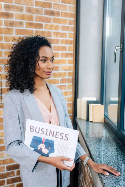 Schöne afrikanisch-amerikanische Gelegenheitsunternehmerin hält Zeitung im Loft-Büro — Stockfoto