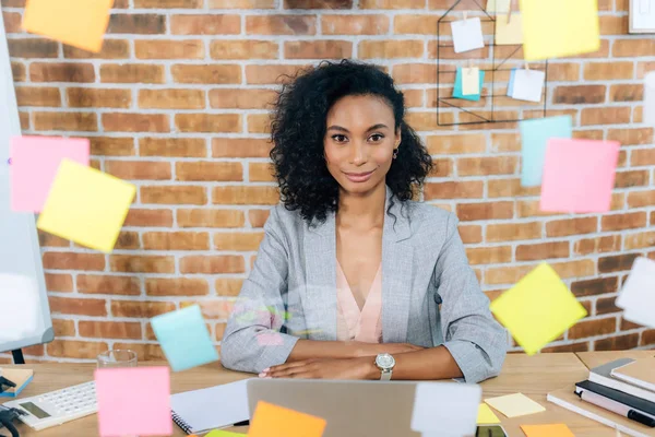 Casual african american businesswoman sitting at desk in front of glass window with Sticky Notes — Stock Photo