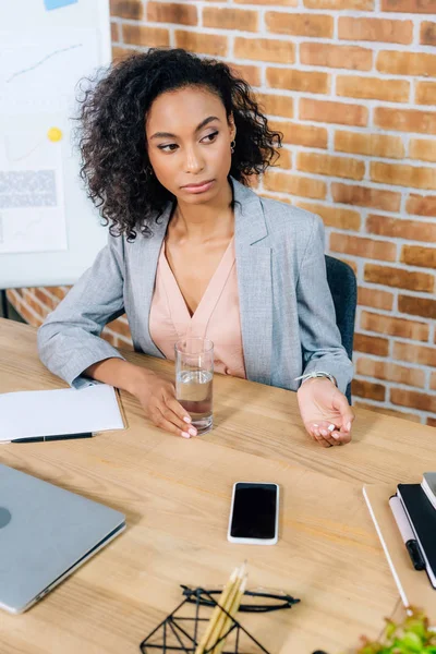Beautiful african american Casual businesswoman with pills and glass of water at office desk — Stock Photo