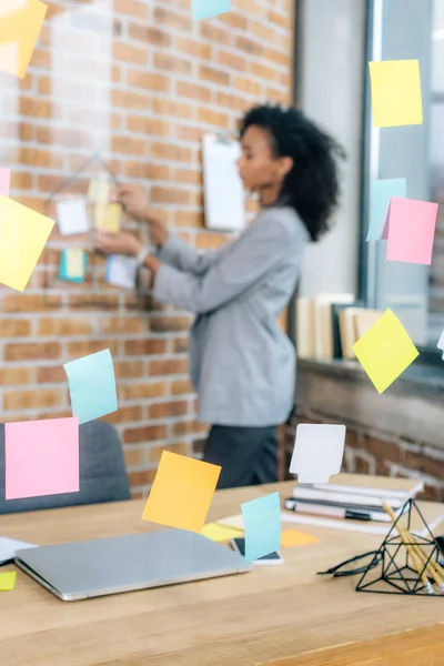 Selective focus of Sticky Notes on glass window near african american Casual businesswoman in office — Stock Photo