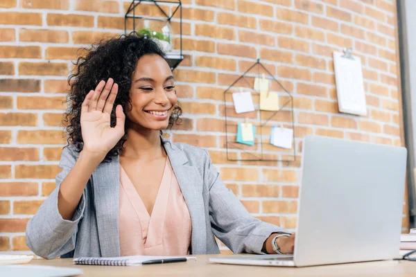 Souriant afro-américain femme d'affaires occasionnelle utilisant un ordinateur portable tout en ayant le chat vidéo — Photo de stock