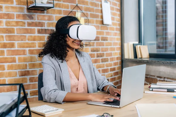 African american Casual businesswoman in virtual reality headset at office desk using laptop — Stock Photo