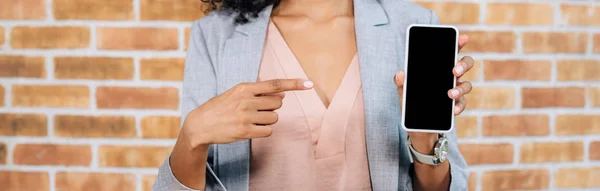 Panoramic shot of african american Casual businesswoman pointing with finger at smartphone with blank screen — Stock Photo