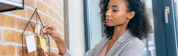 Panoramic shot of Casual african american businesswoman hanging Sticky Notes with pins in loft office — Stock Photo