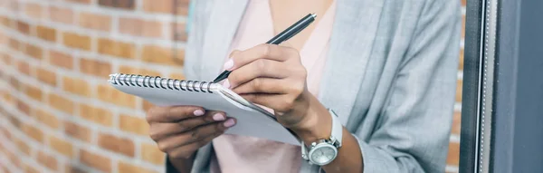 Plan panoramique de femme d'affaires afro-américaine occasionnelle écrivant dans un carnet dans le bureau loft — Photo de stock