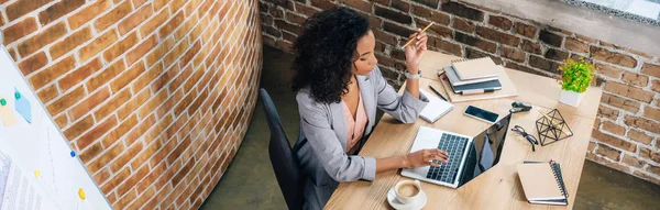 Panoramic shot of african american Casual businesswoman sitting at desk and using laptop — Stock Photo