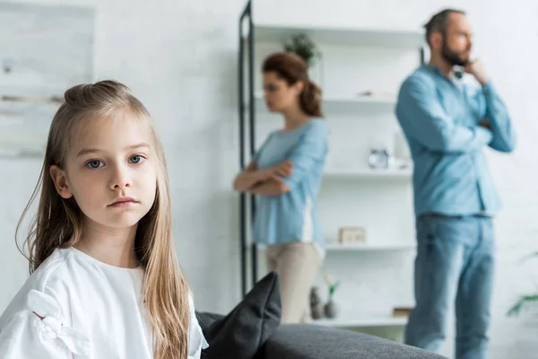 Selective focus of sad kid looking at camera near quarreling parents at home — Stock Photo