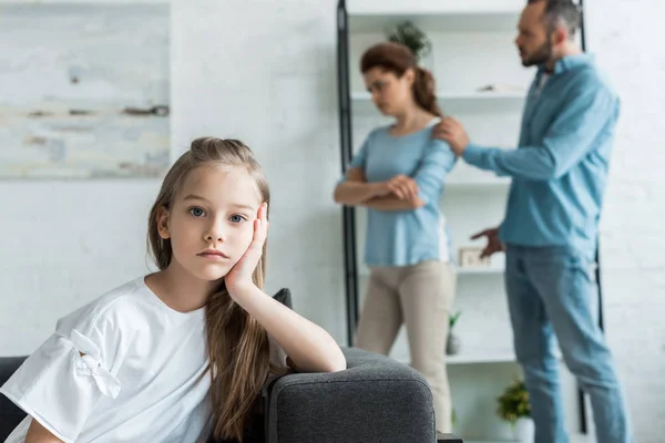 Selective focus of frustrated kid looking at camera near quarreling parents at home — Stock Photo