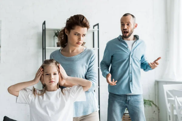 Messa a fuoco selettiva della madre che copre le orecchie sulla figlia mentre l'uomo urla a casa — Foto stock