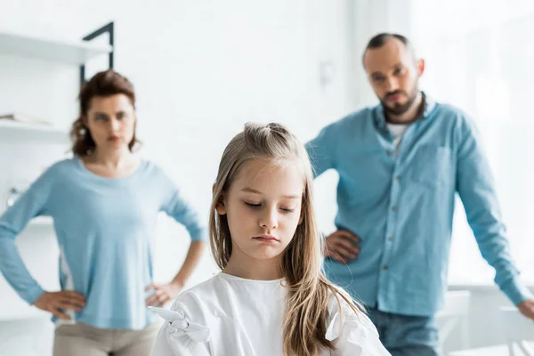 Enfoque selectivo de niño molesto cerca de padres tristes de pie en casa - foto de stock