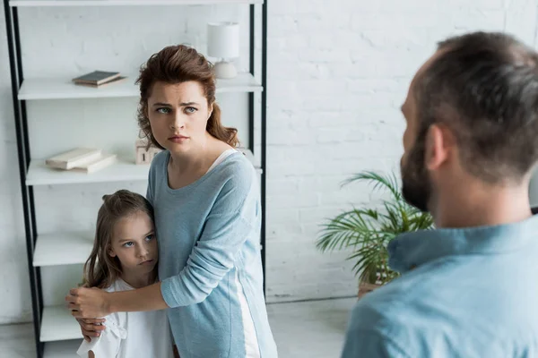 Messa a fuoco selettiva di madre spaventata abbracciando figlia e guardando il marito — Foto stock