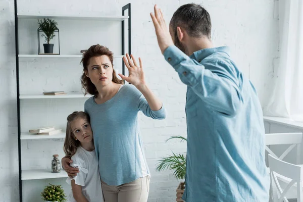 Selektiver Fokus der verängstigten Mutter, die gestikuliert, während sie ihren wütenden Ehemann zu Hause ansieht — Stockfoto