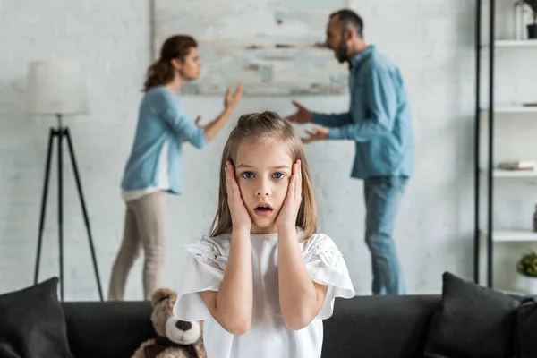 Messa a fuoco selettiva del bambino scioccato toccare il viso mentre in piedi vicino ai genitori litiganti — Foto stock