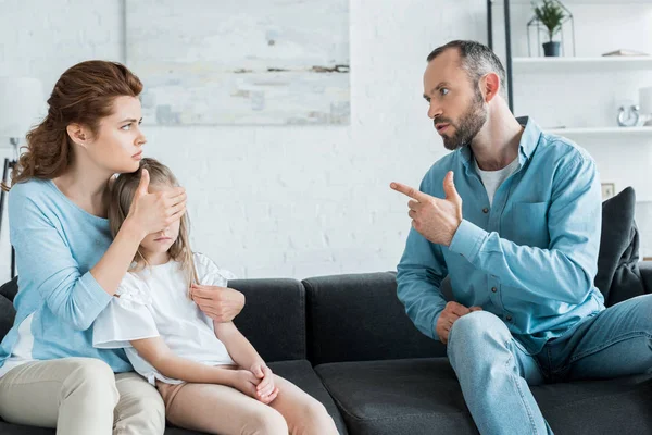 Bearded man pointing with finger at wife while sitting on sofa — Stock Photo