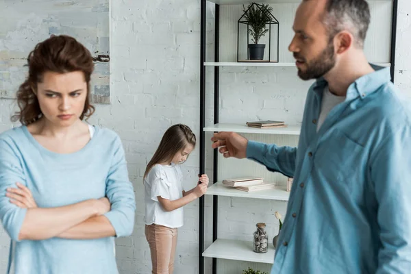 Selective focus of upset kid standing near rack while father pointing with finger near mother — Stock Photo