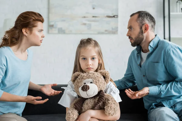 Selective focus of upset kid holding teddy bear near quarreling parents — Stock Photo