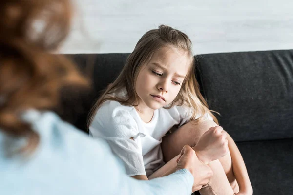 Messa a fuoco selettiva del bambino spaventato seduto sul divano vicino alla madre che si tiene per mano — Foto stock