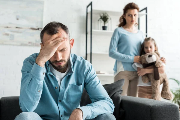 Selective focus of upset man near wife and daughter with teddy bear — Stock Photo