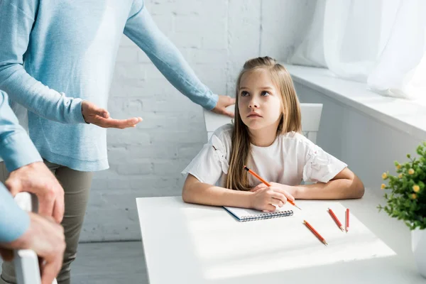 Vue recadrée des parents près d'enfant triste tenant crayon à la maison — Photo de stock