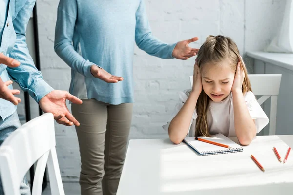 Cropped view of parents near upset kid with closed eyes covering ears — Stock Photo