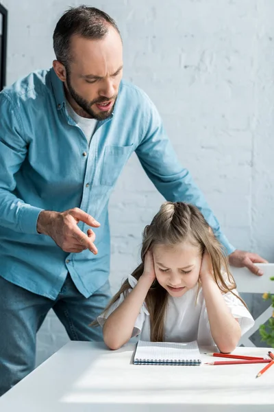 Angry father pointing with finger at notebook near daughter with closed eyes covering ears — Stock Photo