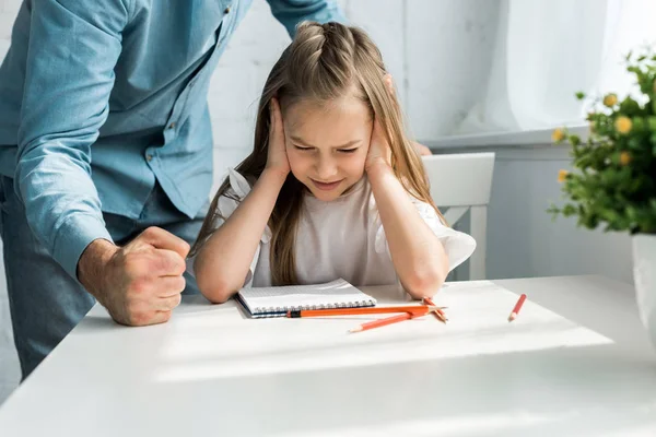 Vista ritagliata del padre che colpisce scrivania con pugno vicino bambino spaventato con gli occhi chiusi a casa — Foto stock