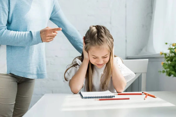 Vista recortada de la madre de pie cerca de niño asustado con los ojos cerrados cubriendo las orejas - foto de stock