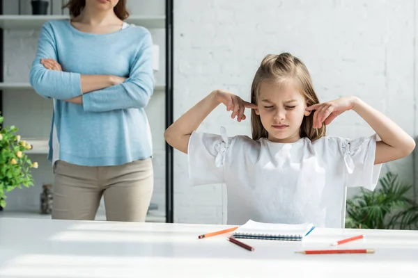 Abgeschnittene Ansicht einer Frau, die mit verschränkten Armen in der Nähe eines Kindes steht und zu Hause Ohren verdeckt — Stockfoto