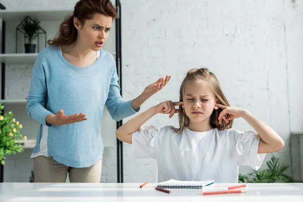 Upset mother gesturing while talking near daughter with closed eyes — Stock Photo