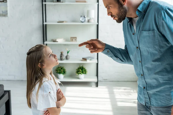 Niño molesto de pie con los brazos cruzados y mirando enojado padre - foto de stock